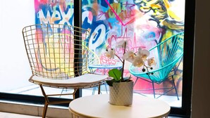 Una habitación con una mesa redonda, dos sillas de alambre y un ventanal con grafitis de colores.