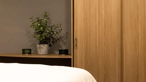 Un dormitorio con un armario de madera, una mesita de noche con una planta en maceta y dos pequeños recipientes.