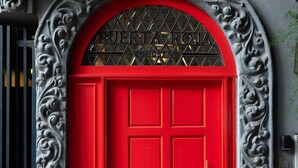 Una puerta roja con un arco decorativo y un letrero de metal encima.