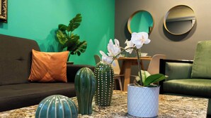 Una sala de estar con una pared verde, un sofá gris, una mesa de centro con jarrones decorativos y una mesita con una planta.