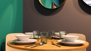 Mesa de comedor dispuesta con fuentes, platos y cubiertos blancos, rodeada de paredes azul aguamarina y un espejo.