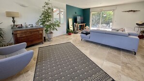 Un salon comprenant un canapé, des fauteuils, une table basse, un téléviseur et une grande fenêtre.