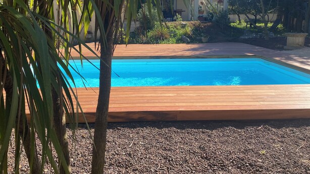 Une piscine entourée d’une terrasse en bois, de gravier et de palmiers.