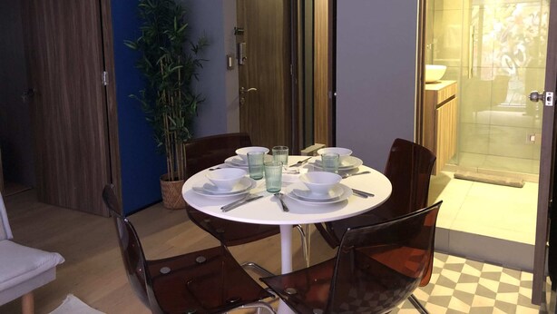 A dining area with a round table set for four, surrounded by chairs. There is a potted plant to the left and a glass door leading to a bathroom. - Terraza, Diseño y Ubicacion  en la Condesa (Ciudad de México)