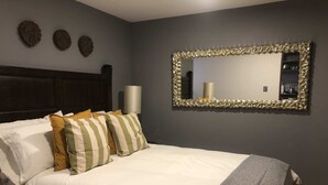 A neatly made bed with striped pillows, a large mirror with a decorative frame, and a wall-mounted light fixture. - Terraza, Diseño y Ubicacion  en la Condesa (Ciudad de México)