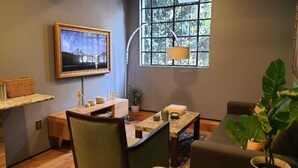 A cozy living room with a TV mounted on the wall, a dining table, chairs, a large window with a view of trees, and a potted plant. - Terraza, Diseño y Ubicacion  en la Condesa (Ciudad de México)