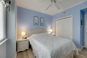 Ein Schlafzimmer mit einem Bett, Nachttischen, einem Deckenventilator und zwei gerahmten Bildern an der Wand.