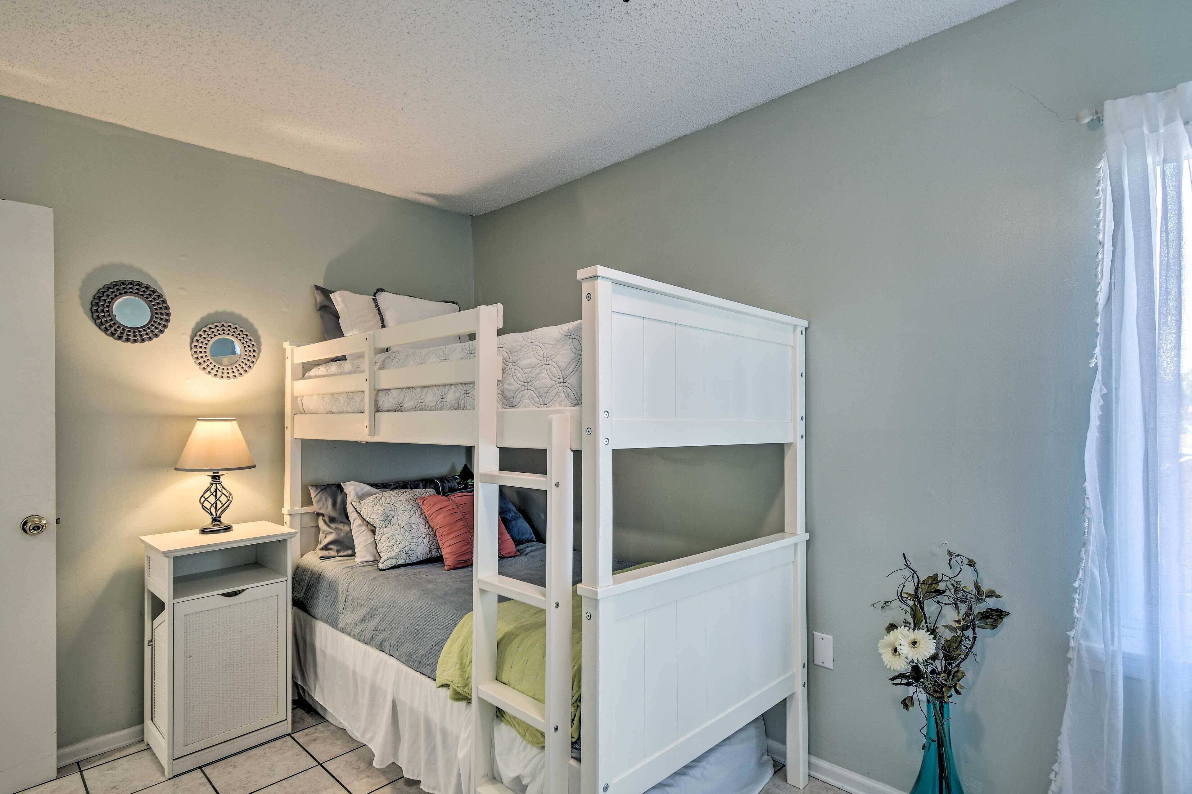 A bunk bed room with a nightstand, a lamp, and a vase with flowers.