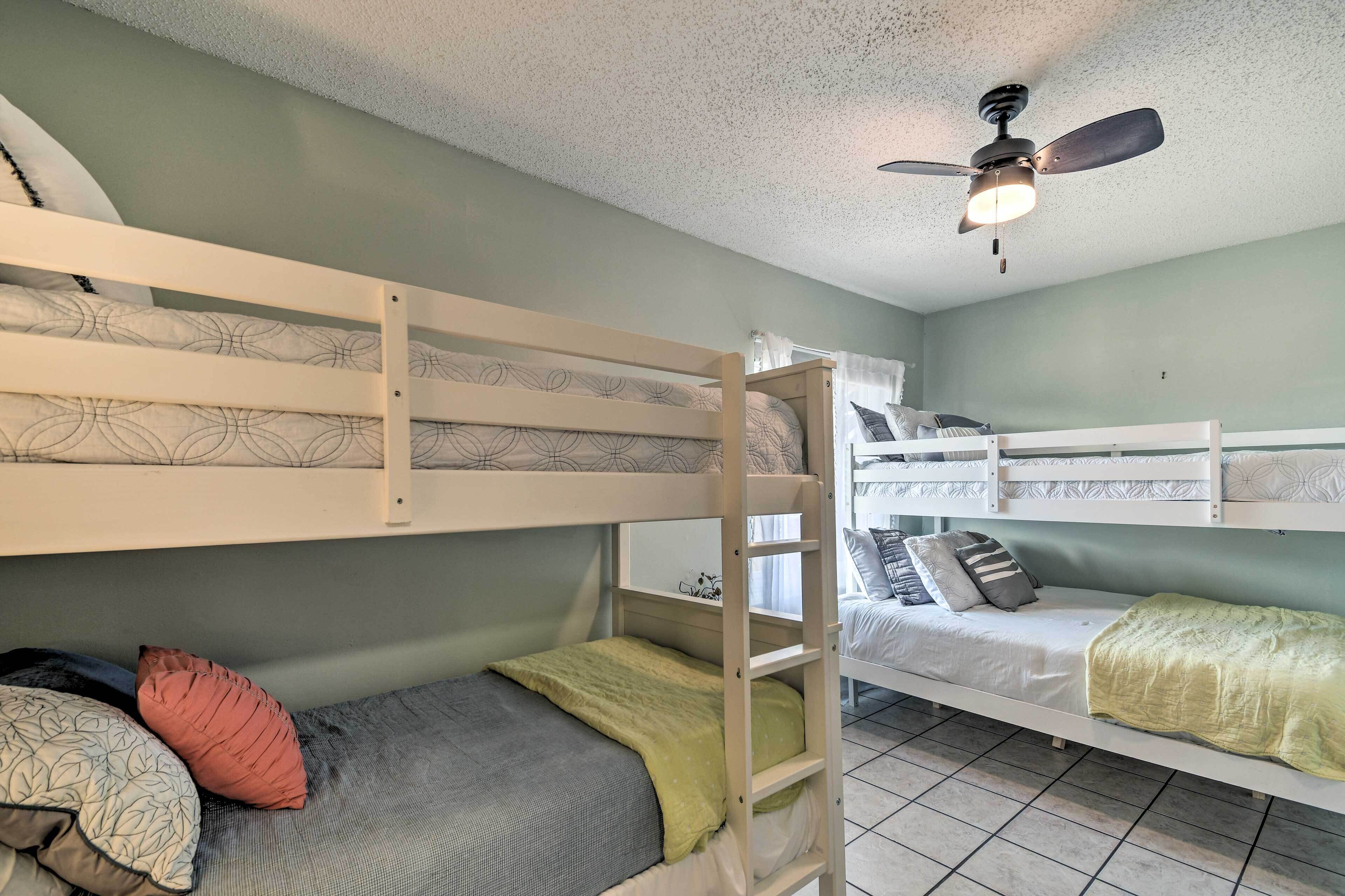 A bunk bed room with a ceiling fan, a window with curtains, and a tiled floor.