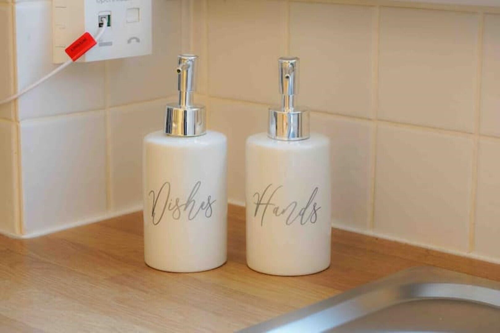 Two white bottles with silver tops labeled "Dishes" and "Hands" on a kitchen counter.