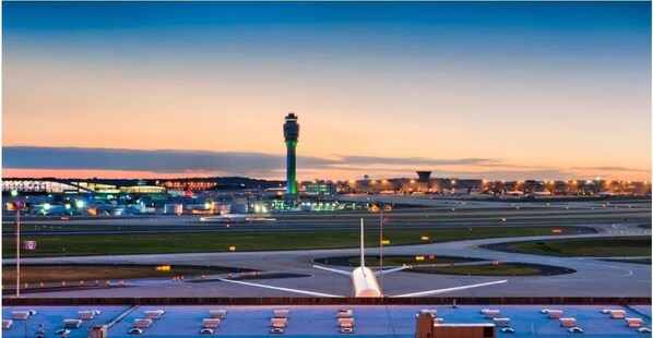 An airport runway with a control tower and terminal buildings in the background.
