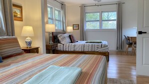 A bedroom with a bed, bedside tables, a desk, and a chair. There are windows with curtains, a ceiling fan, and a door. - Newly Renovated Cozy Rustic Home l 10 min from Truist Park (Smyrna)