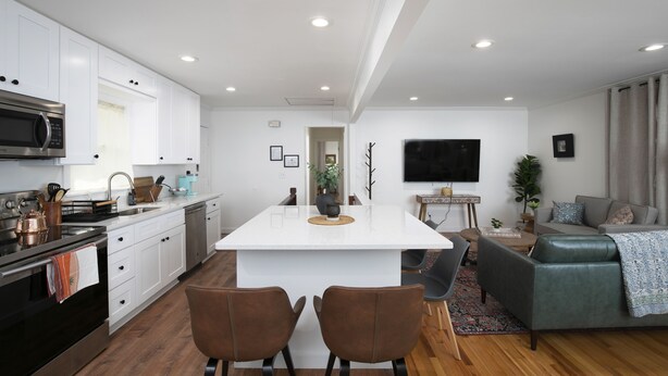 A modern kitchen with white cabinets, a central island, and a dining area with two chairs. - Newly Renovated Cozy Rustic Home l 10 min from Truist Park (Smyrna)