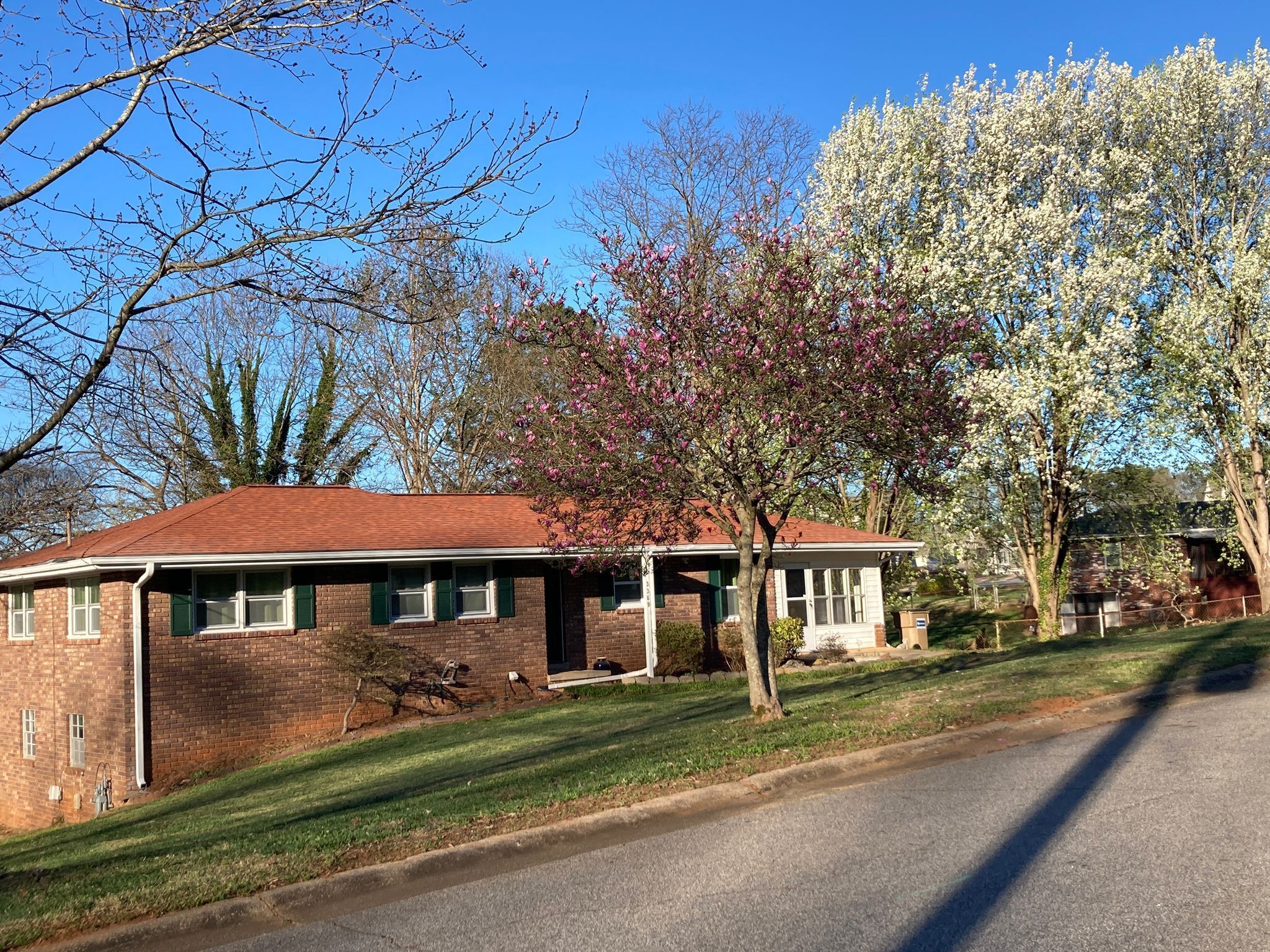A single-story brick house with a red roof, a front porch, and a small front yard.