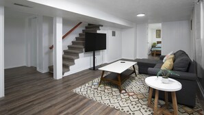 A modern living room with a staircase, a flat-screen TV, a grey sofa, and a patterned rug. - Newly Renovated Cozy Rustic Home l 10 min from Truist Park (Smyrna)