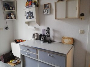 A kitchen with a white countertop, grey cabinets, a coffee maker, a kettle, and a clock on the wall. - Old apartment in top location (Leipzig)