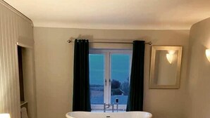 Une chambre avec un grand lit, une baignoire et une vue sur l’extérieur.