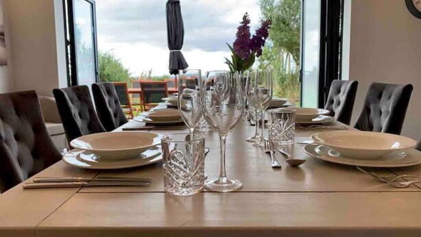Une table à manger dressée pour un repas, avec des chaises, des assiettes, des couverts et des verres à vin.