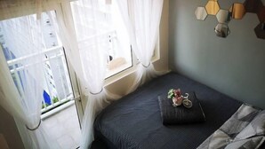 A small, neatly arranged bedroom with a bed, a window with sheer curtains, a wall-mounted light fixture, and a small decorative item on the bed. - SM Mall of Asia MOA NAIA Pasay Staycation SMX Convention PICC World Trade Center (Pasay)