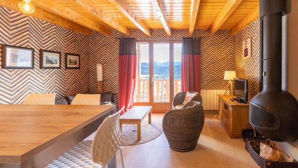 A cozy cabin interior with a wooden ceiling, a dining area, a sofa, a TV, and a fireplace. - Le Caribou - Appt 3 chambres proche pistes (Les Angles)
