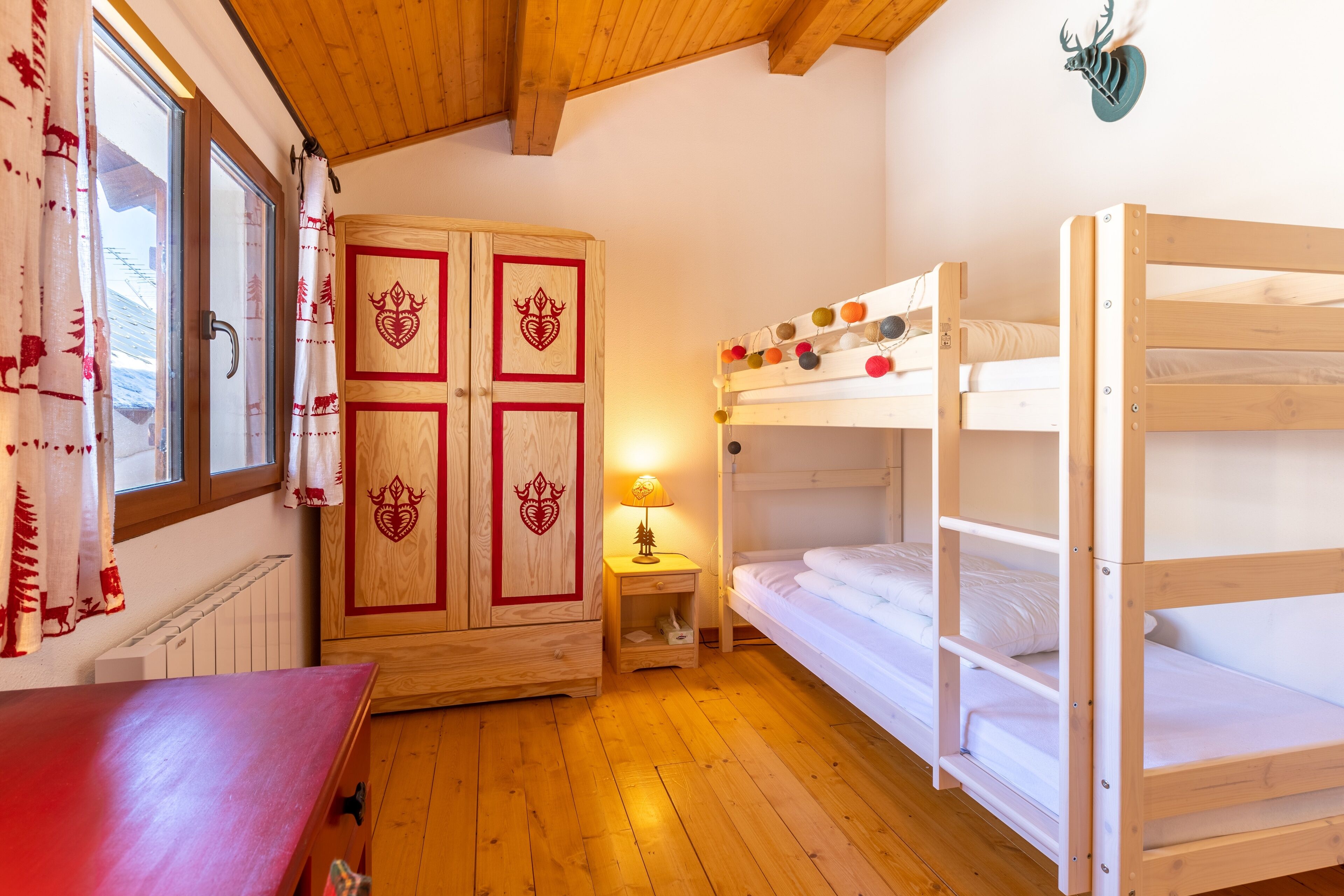 A room with a bunk bed, wooden wardrobe, and a table.