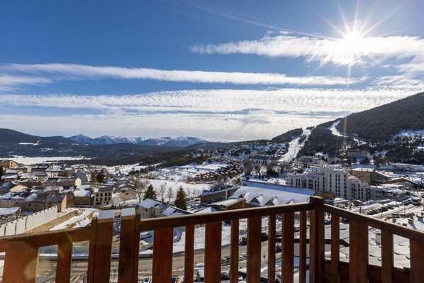A panoramic view of a town with snow-covered streets and buildings, a clear sky, and mountains in the background.