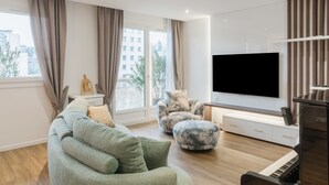 A modern living room with a sectional sofa, a marble-patterned ottoman, a flat-screen TV, and a piano.