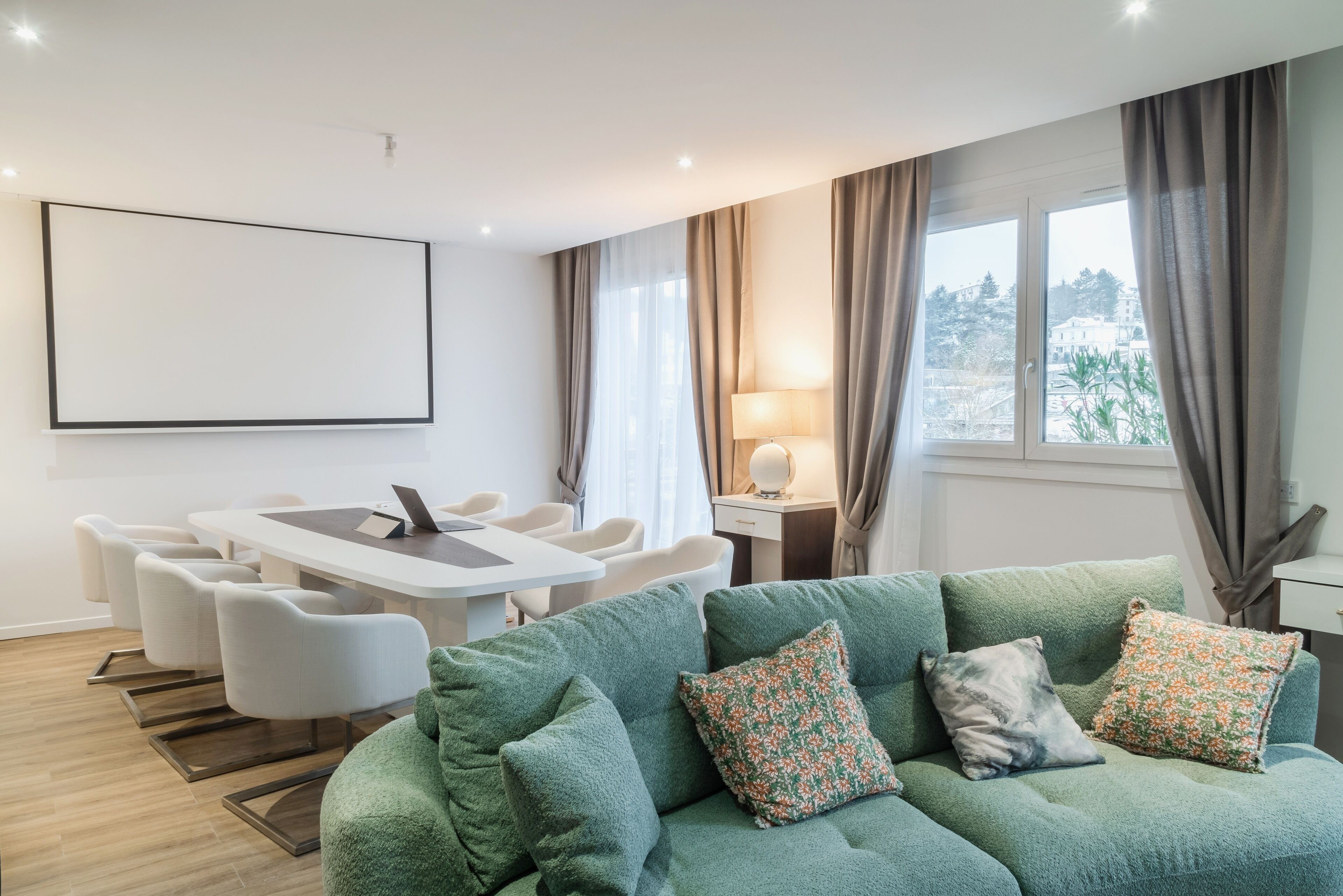Una sala de estar moderna con un sofá verde, una mesa de comedor con sillas, un televisor y vista a la ciudad por la ventana.