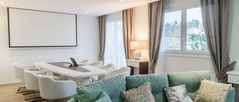 Una sala de estar moderna con un sofá verde, una mesa de comedor con sillas, un televisor y vista a la ciudad por la ventana.