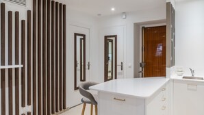 A modern kitchen with a white countertop, wooden vertical blinds, and a grey chair.