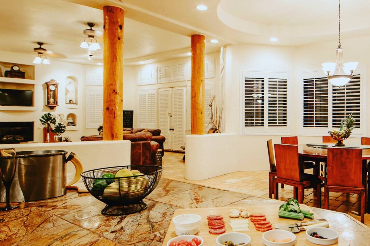 A spacious living area with a wooden dining table set for a meal, surrounded by comfortable seating and a large window with shutters.