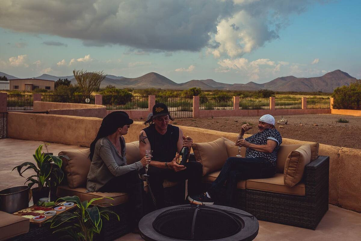 A group of people sitting on outdoor sofas with a view of mountains and a cloudy sky.