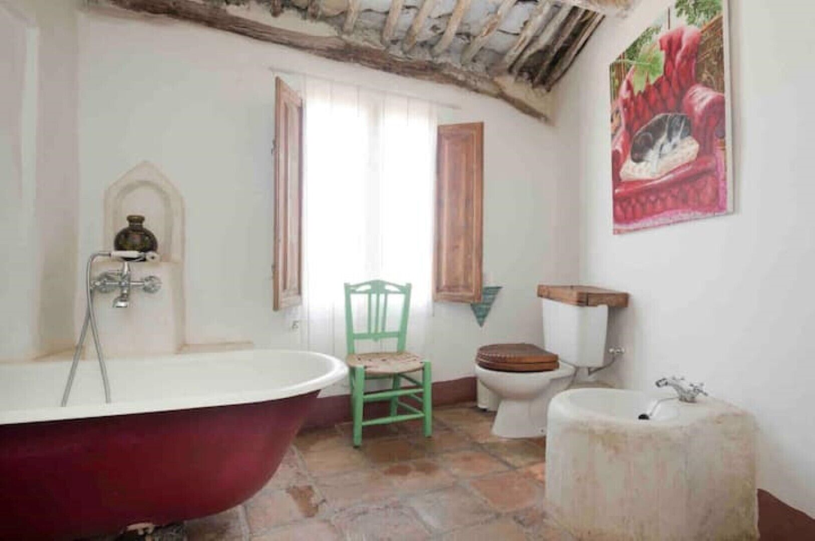 Une salle de bain avec une baignoire sur pieds, une chaise en bois, des toilettes et un lavabo.