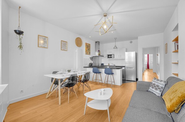 Una cocina moderna con una isla central, paredes blancas y una zona de comedor con mesa y sillas blancas.
