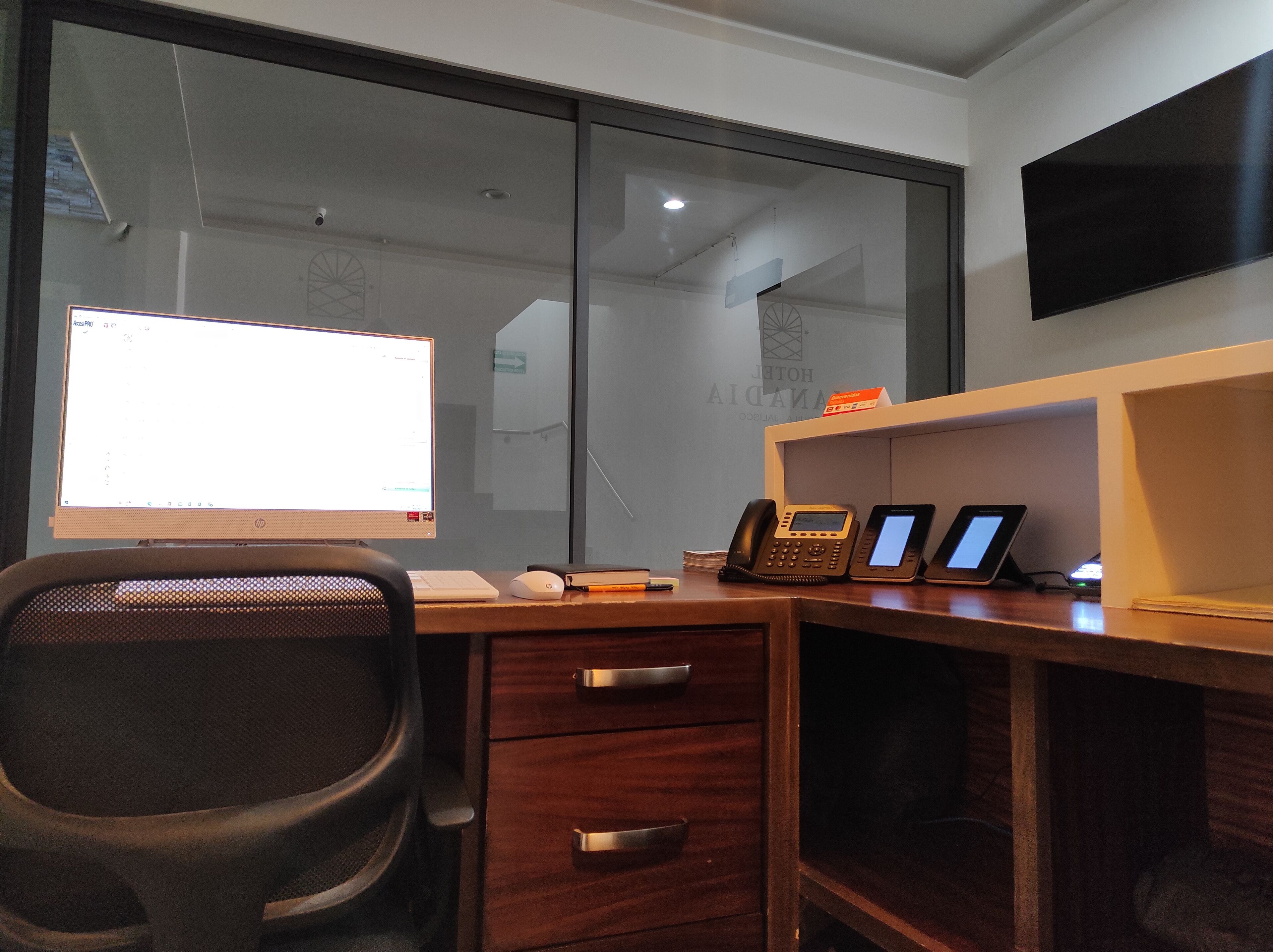 Escritório de hotel com um computador de mesa, um telefone e uma TV de tela plana em uma mesa.
