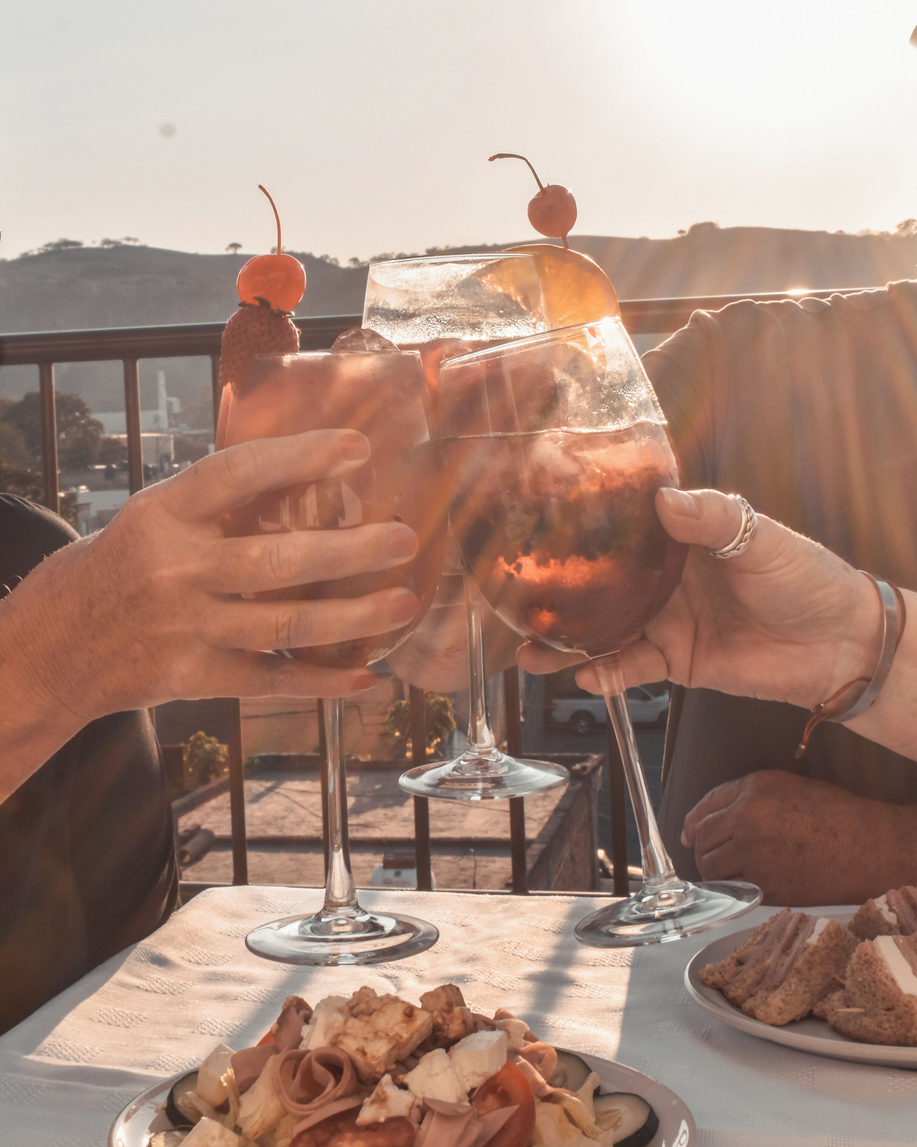 Two people toasting with drinks at a table with food and a scenic view.