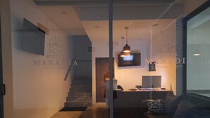 Uma área de recepção de hotel com um balcão, uma televisão fixada na parede e uma escada que leva a outro andar.