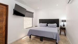 Um quarto moderno com cama, televisão de tela plana na parede, mesa de cabeceira com abajur e janela com persianas.