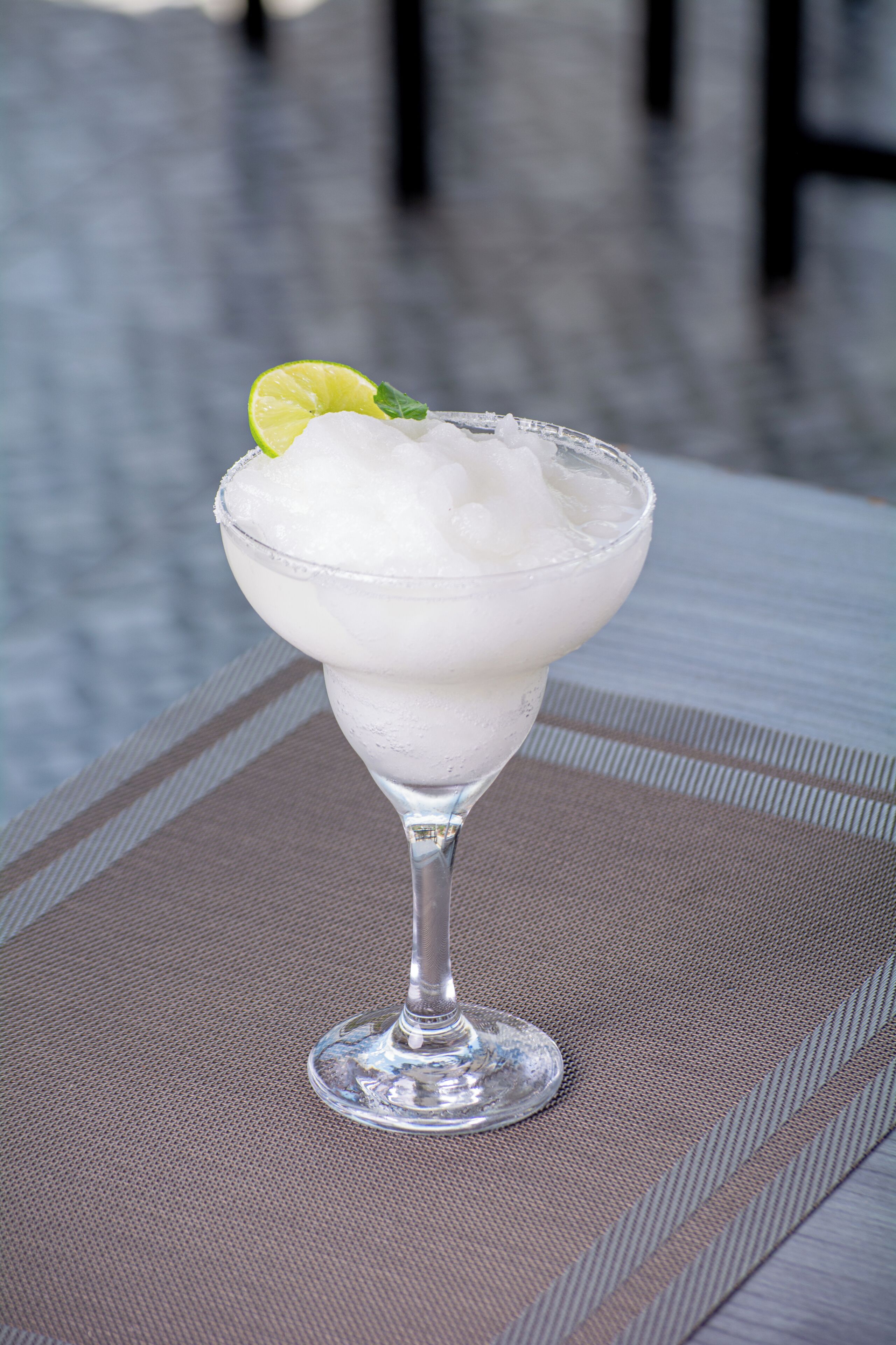 A cocktail in a stemmed glass with ice and a lime garnish on a textured table.