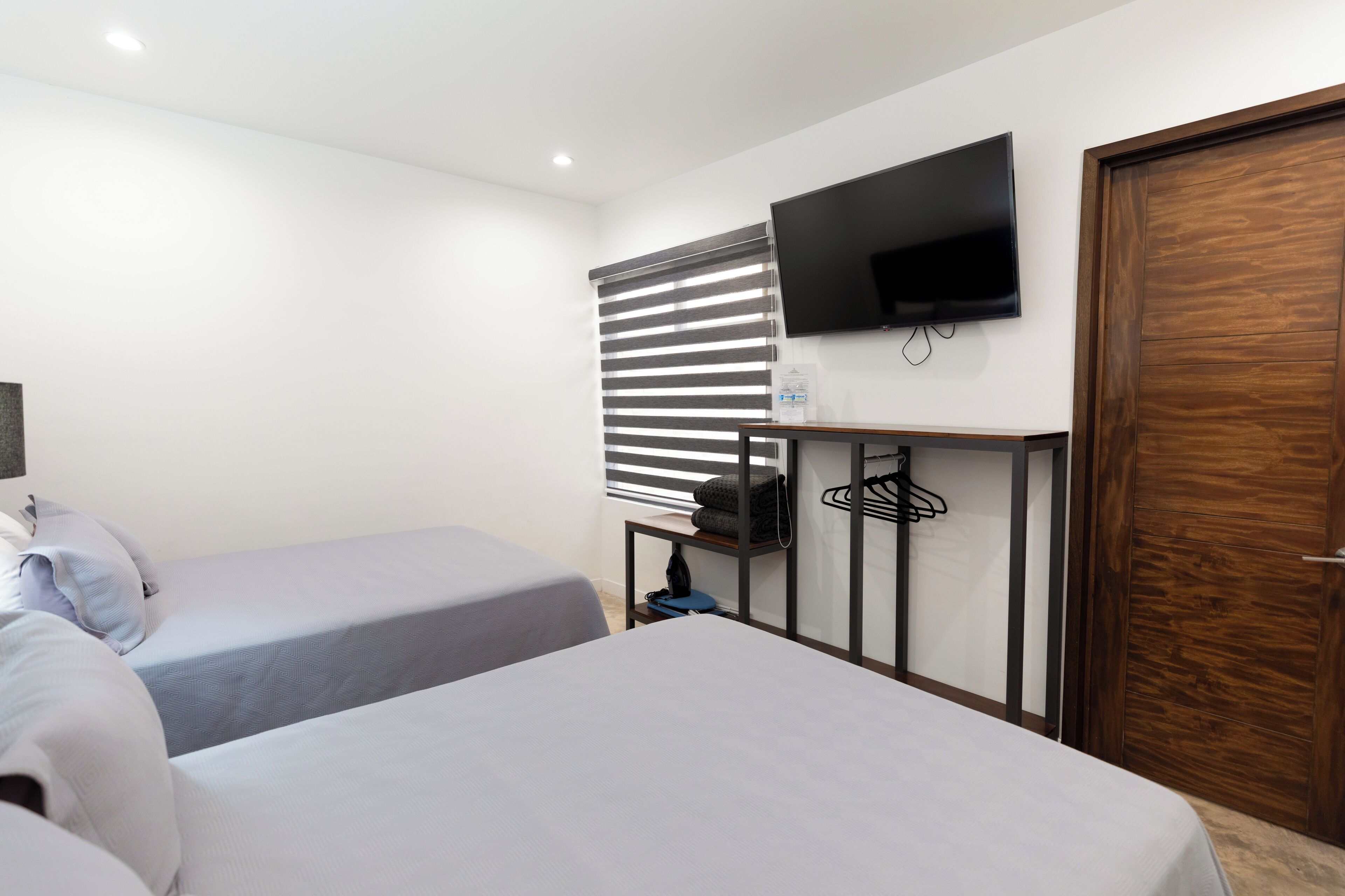 Una habitación con dos camas, un televisor montado en la pared y una puerta de madera.