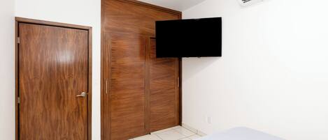 Ein Schlafzimmer mit einem Holzkleiderschrank, einem Wand-Fernseher und einem weißen Bett.