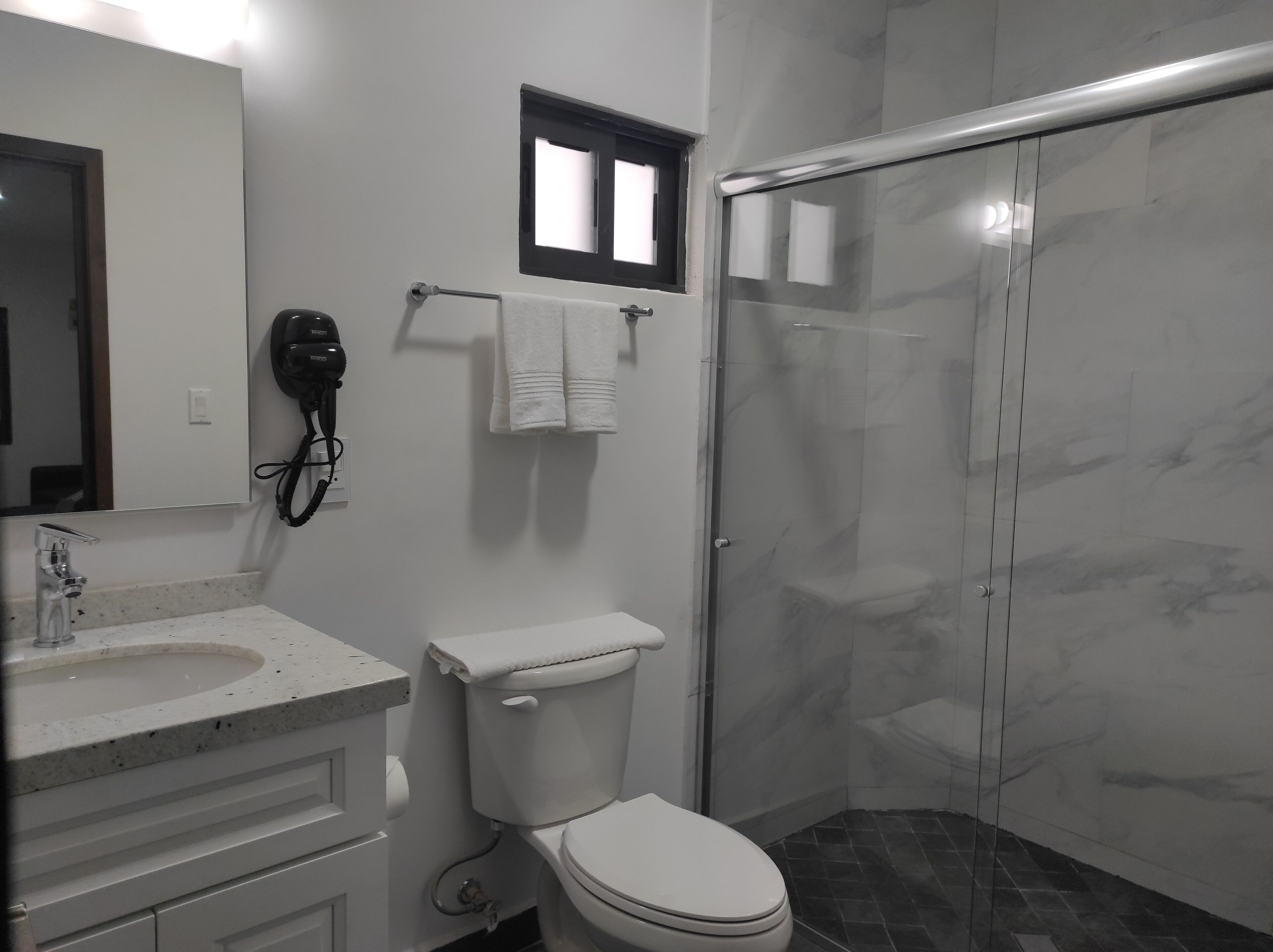 A bathroom with a toilet, sink, and a hairdryer mounted on the wall.