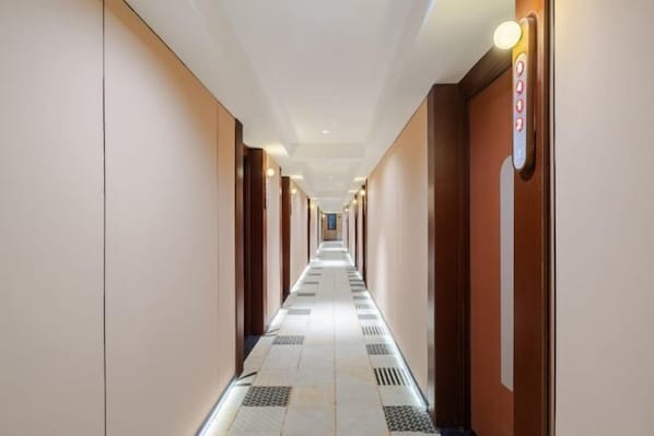A long, narrow hotel corridor with a tiled floor, wooden doors, and a light fixture on the wall.
