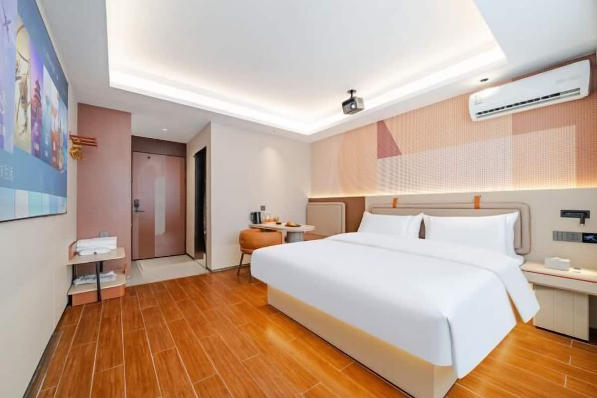 Une chambre d’hôtel moderne avec un grand lit, des tables de chevet, un petit coin salon et un luminaire au plafond.