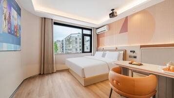 Quarto de hotel com cama, escrivaninha, cadeira, janela com vista para edifícios e luminária no teto.