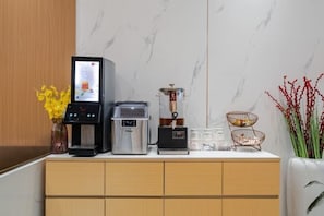 Un minibar con cafetera, dispensador de té y una jarra de vidrio sobre una encimera de mármol.