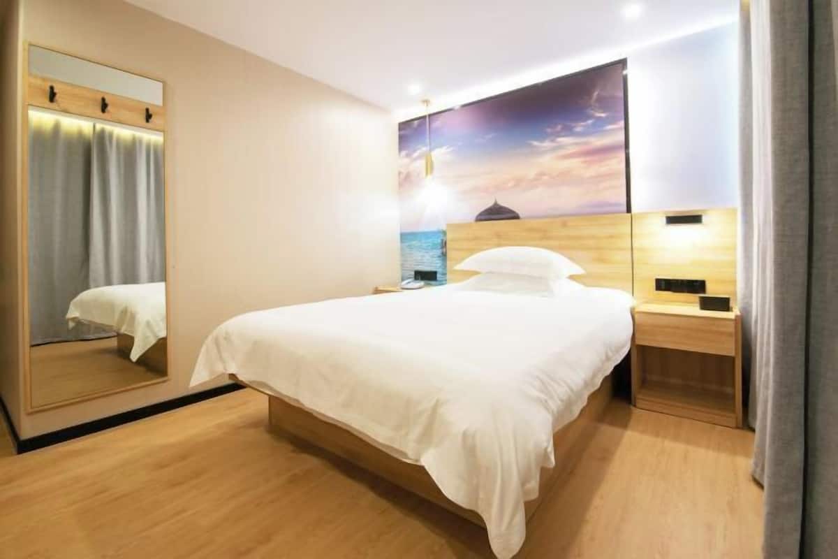 Une chambre d’hôtel moderne avec un grand lit, une table de chevet, une commode, un miroir et un téléviseur fixé au mur.