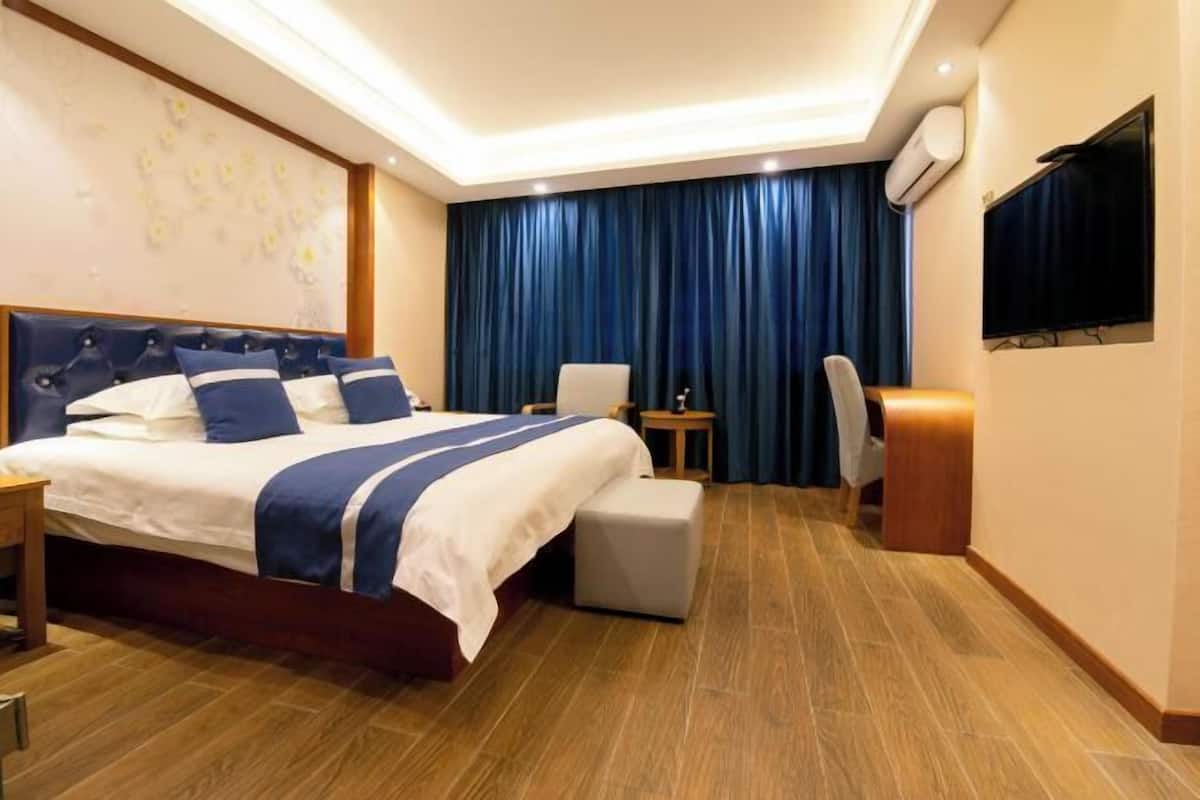 Une chambre d’hôtel avec un grand lit, un bureau, une chaise, une télévision et une fenêtre avec des rideaux.