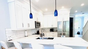 A modern kitchen with white cabinetry, a central island with bar stools, stainless steel appliances, and blue pendant lights. - Islamorada Florida Bay Villa  Plunge Pool, Boat Dock, Amazing Sunset Views (Islamorada)