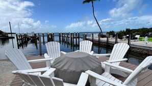 A deck with white Adirondack chairs and a round table, overlooking a marina with boats and a clear sky. - Islamorada Florida Bay Villa  Plunge Pool, Boat Dock, Amazing Sunset Views (Islamorada)